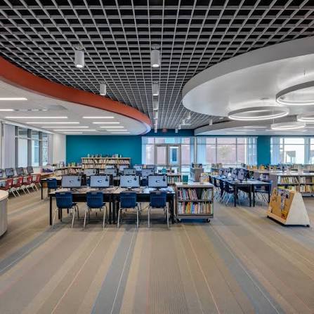 Library bookshelves and learning areas beneath sculptural ceiling panels at Sonia Sotomayor Elementary School